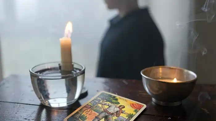 Расклад Таро на одну карту на отношения с пасынком — карта Повешенный на столе с символами тишины и размышлений